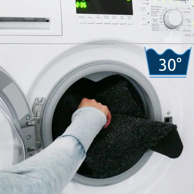 Persona che inserisce la footmat your GEAR Mantua per gradino camper in una lavatrice; simbolo 30° indica che il tappetino per gradini 55x28 cm è lavabile in lavatrice a 30 gradi.