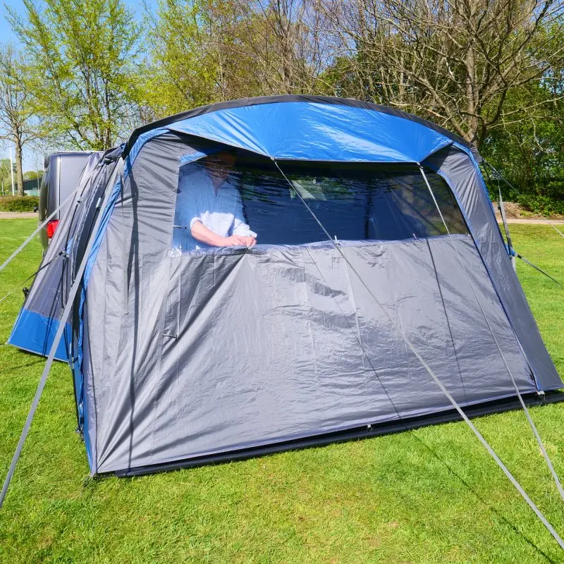 Vorderwand mit Fenster und Zeltboden des yourGEAR Panarea 320 Zubehörsets, montiert an einem Busvorzelt auf einer Wiese; graues 150D Oxford Polyester mit Reißverschluss und blickdicht verschließbarem Fenster.