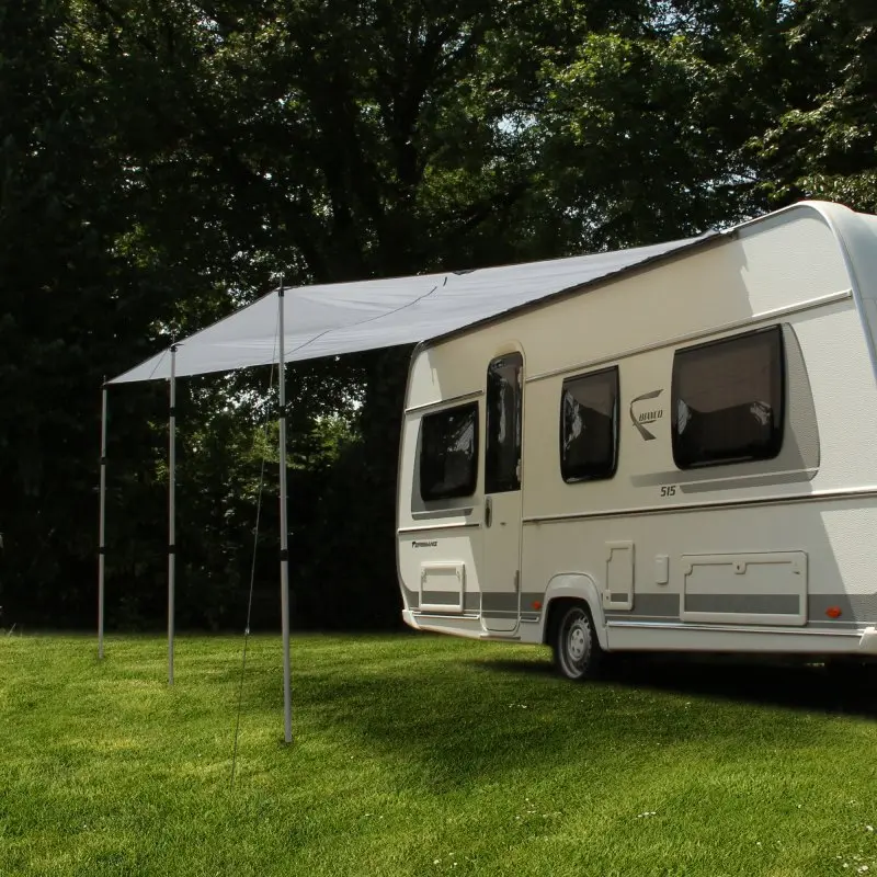 Toldo para caravana yourGEAR 3 x 2,4 m en gris, instalado en un remolque, con tres postes telescópicos de aluminio, proporcionando sombra y protección solar UV 50+ en un entorno de camping.