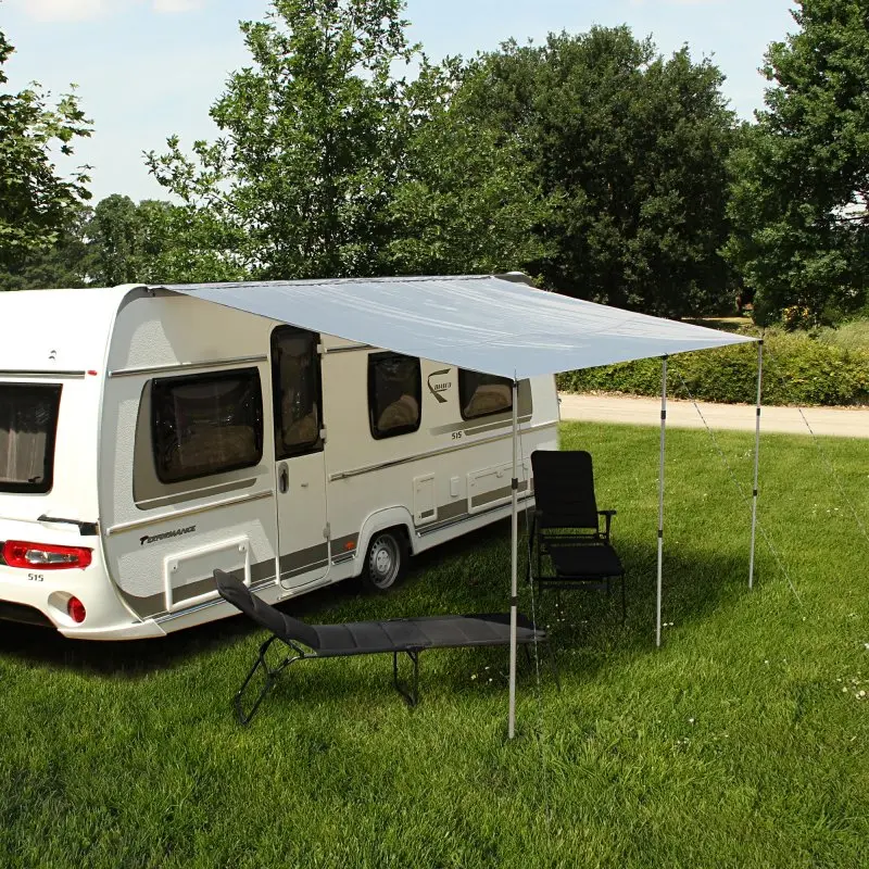 Toldo para caravana your GEAR de 4,5 x 2,4 m en color gris, montado con tres postes telescópicos de aluminio, proporciona sombra y protección UV junto a una caravana estacionada en césped.