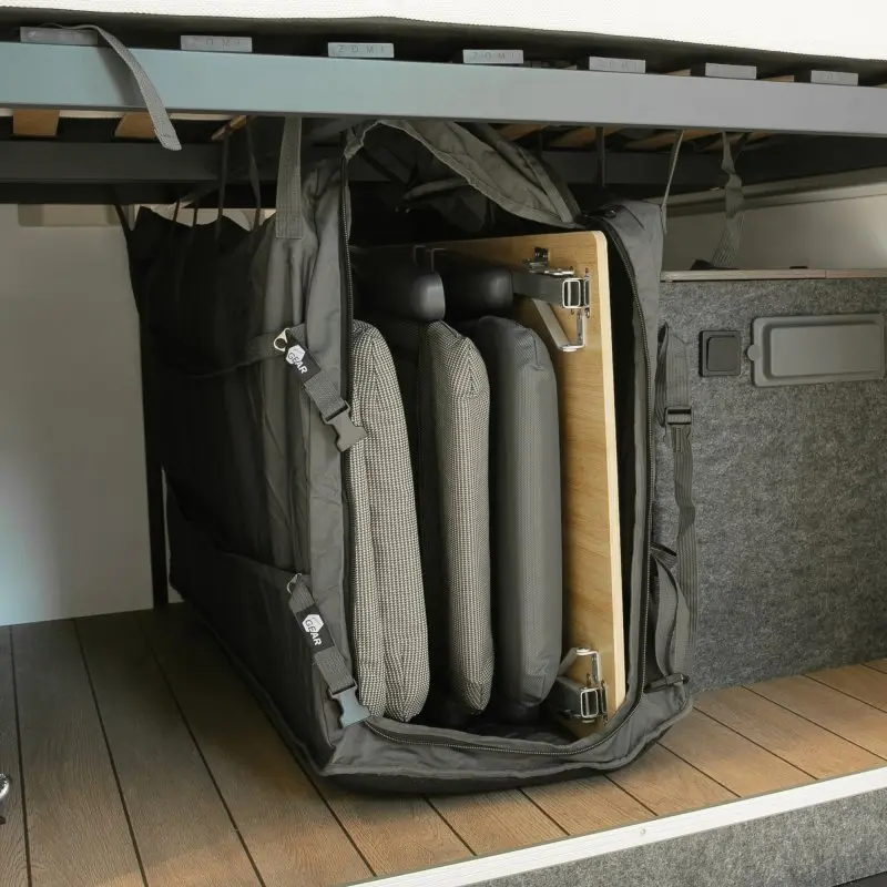 Borsa organizer your GEAR Bozen per mobili da campeggio, fissata verticalmente nella zona garage di un camper, con sedie e tavolo pieghevoli all’interno, materiale robusto e cinghie di sicurezza visibili.