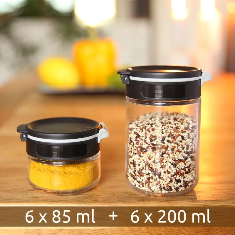 Two your GEAR Double-Flip spice jars made of glass, one 85 ml and one 200 ml, with black lids and transparent bodies, displayed on a wooden kitchen surface with spices inside. Text shows “6 x 85 ml + 6 x 200 ml”.