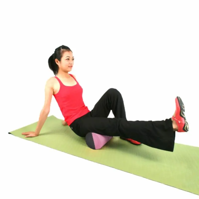 Mujer usando la Carnegie EVA Pilatesrolle de 90x15 cm sobre una colchoneta verde, realizando automasaje en la pierna; rodillo cilíndrico violeta ideal para yoga, pilates y liberación miofascial.
