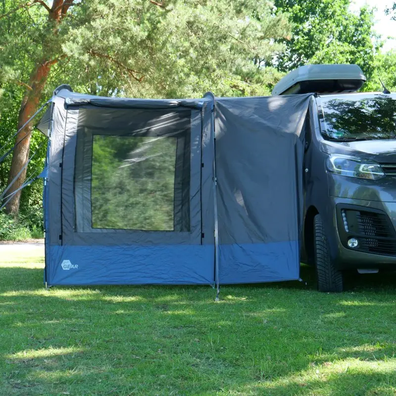 Auvent your GEAR Panarea 320 gris et bleu, monté sur un van, grande fenêtre frontale, tissu imperméable, protection UV 50+, structure légère, installé sur pelouse en plein air.