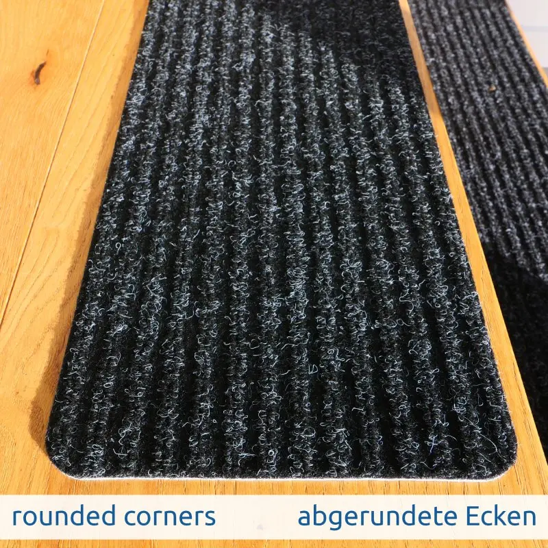 Tapis de marche yourGEAR gris foncé 76x20cm, surface structurée antidérapante, coins arrondis, dessous TPR auto-adhésif, posé sur une marche en bois, idéal pour sécuriser les escaliers.
