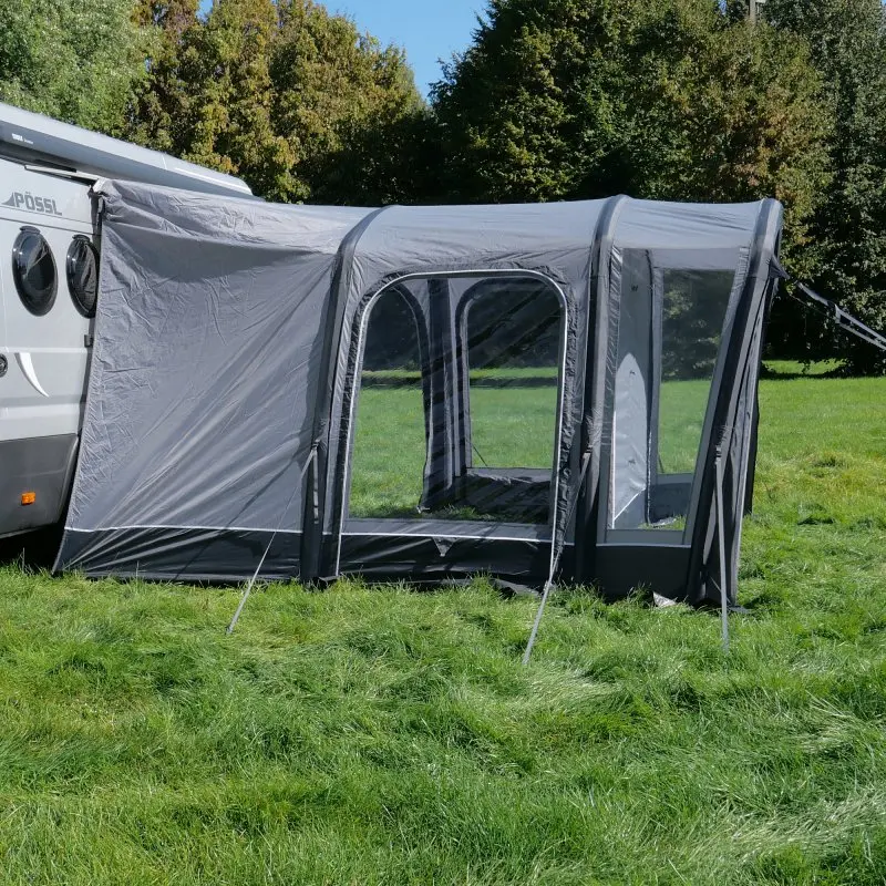 Avance de aire your GEAR Manarola para furgoneta camper, color gris, 320 x 325 cm, con grandes ventanas transparentes y puerta lateral, instalado junto a un vehículo en un entorno de césped y árboles.