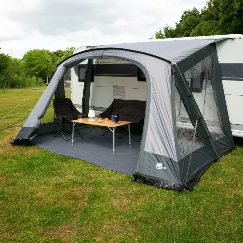 Auvent your GEAR Positano 330 pour caravane, gris, avec 4 grandes fenêtres transparentes, large porte frontale, armature en aluminium, installé devant une caravane, mobilier de camping à l’intérieur.