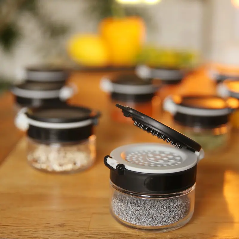 your GEAR Double-Flip spice jar set with black lids, open and closed, on a wooden surface. Glass jars in 85 ml and 200 ml sizes for kitchen spice organization, ideal for herbs and seasonings.