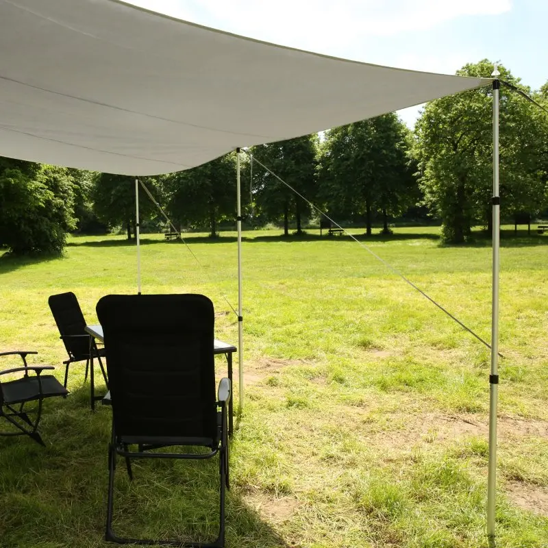 Caravan thermo tarp 435 x 250 cm by your GEAR, opaque and waterproof with UV80 protection, mounted with poles and ropes, providing shade over outdoor camping chairs and table on a grassy area.