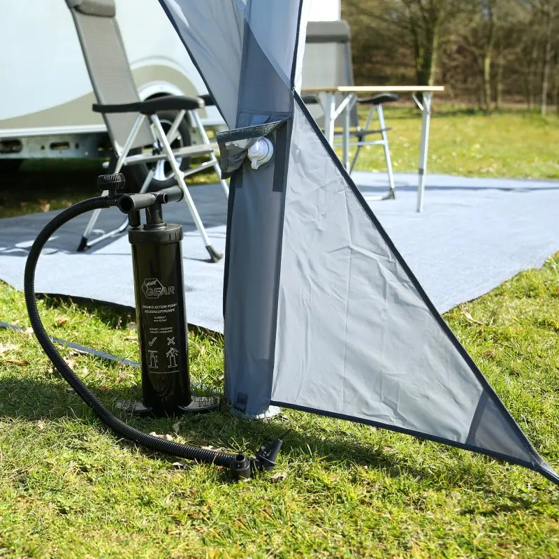 Graues, aufblasbares your GEAR Amalfi Air 450 Caravan Sonnensegel am Wohnwagen, mit Doppelhubpumpe, aufgebaut auf einer Wiese vor Campingmöbeln und Teppich; maßgeschneidert für Hobby Beachy Modelle.
