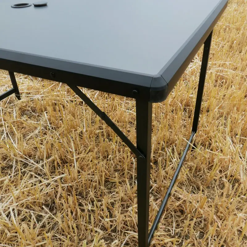 Table de camping your GEAR Tivoli XL, plateau rectangulaire en aluminium noir, pieds pliables robustes, structure légère, résistant à l’eau, facile à transporter, posé sur un champ de blé sec.
