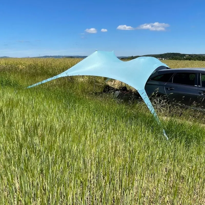 XXL your GEAR Cameo beach shelter 3x3m made of light blue Lycra, set up as a sunshade next to a car on a grassy field, offering UV 50+ protection, ideal for beach, picnic, or outdoor use.