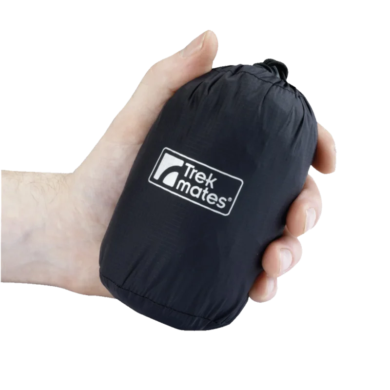 Hand holding a compact, packed Trekmates waterproof and breathable rain jacket with hood, black nylon material, 3000mm water column, visible Trekmates logo on pouch, ideal for outdoor and travel use.