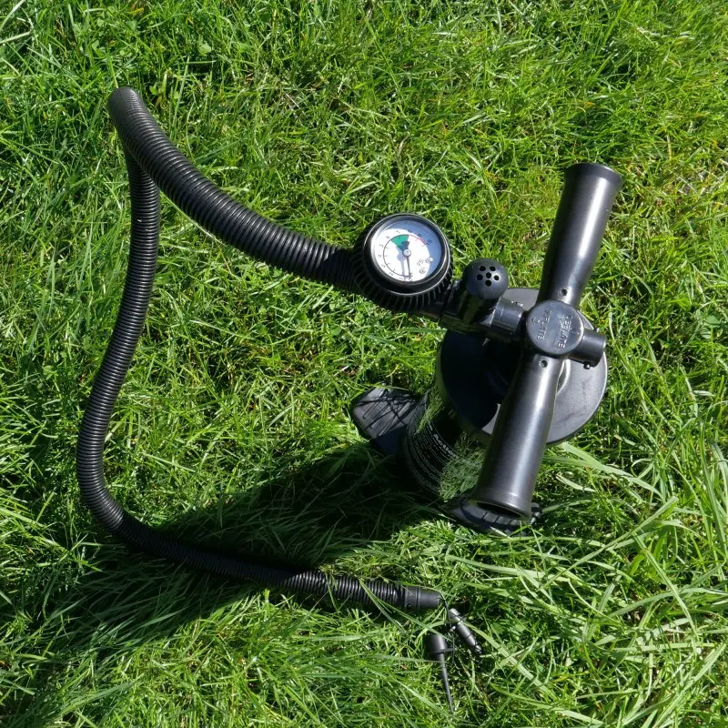 Bomba de aire negra con manómetro y manguera flexible, utilizada para inflar el avancé hinchable your GEAR Manarola Air Camper, fotografiada sobre césped verde. Ideal para camping y autocaravanas.