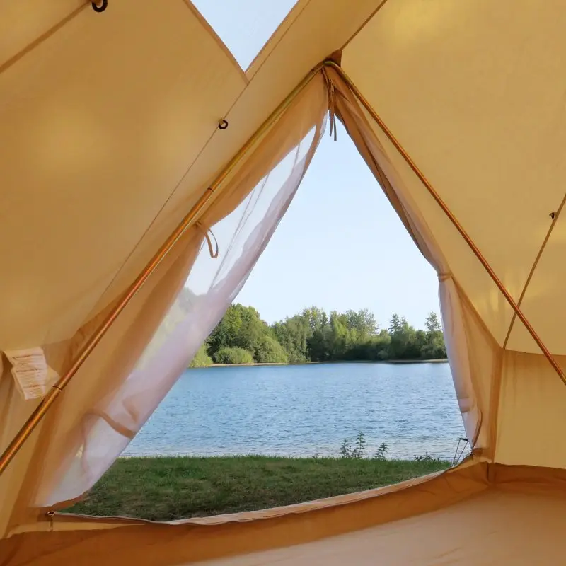 Blick aus dem your GEAR Zelt Desert 8 Pro UV50+ aus Baumwoll-Mischgewebe mit fest vernähter Bodenwanne, Tipi-Form und Insektenschutz auf einen See und grüne Uferlandschaft.