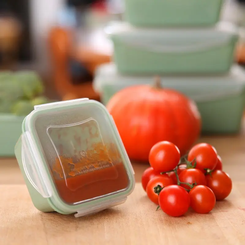 Set de 6 recipientes herméticos your GEAR Pila de 300 ml, apilables y cuadrados, color verde, con tapas transparentes, ideales para conservar alimentos. Tomates frescos y calabaza aparecen junto a un recipiente lleno.