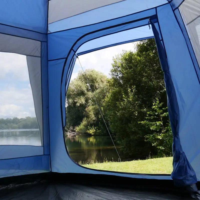 Vue depuis l’intérieur du your GEAR Zelt Ponza 400, grand festivalzelt bleu avec sol cuvette, moustiquaire intégrée et grande ouverture, offrant vue sur un lac et des arbres. Tente spacieuse, idéale pour groupe ou famille.