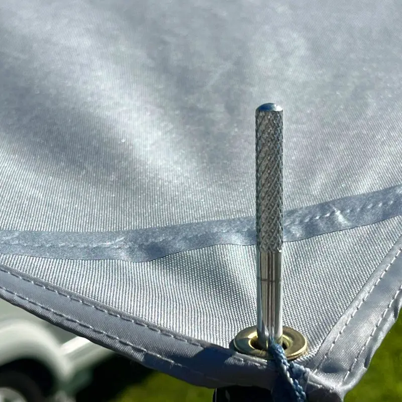 Close-up of your GEAR Caravan Thermo Tarp with silver aluminum-coated Oxford polyester fabric, reinforced seams, metal eyelet, and guyline attachment, showing robust, UV80+ and waterproof sun canopy for caravans.