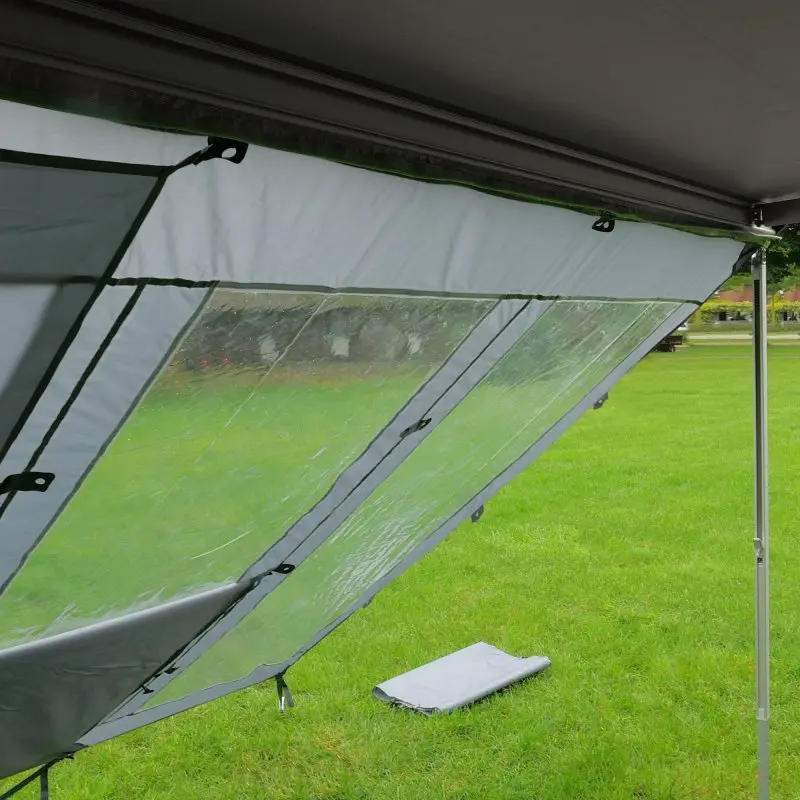 Panel frontal your GEAR Panorama Wall 2,4 x 2 m para toldo, color gris con ventana transparente, protege del sol, viento y lluvia, instalada al aire libre sobre césped. Ideal como protección y visibilidad.