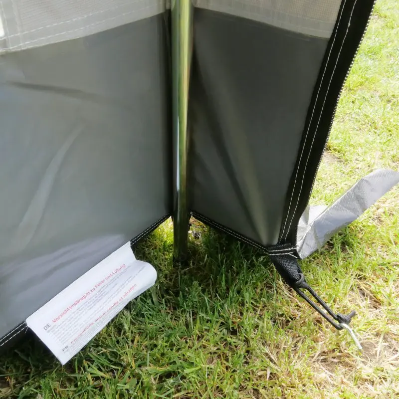 Détail du your GEAR Trient Multi Storage : coin intérieur du tente PVC imperméable, piquet métallique, ourlet renforcé et bande de sol protectrice visible sur herbe, adapté pour stockage ou cuisine extérieure.