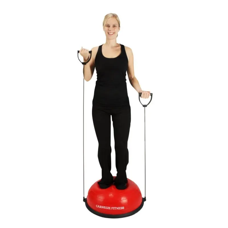 Woman standing on a red Carnegie Fitness balance ball with resistance bands, demonstrating a workout. Balance trainer features sturdy base and attached pull bands for strength and stability exercises.
