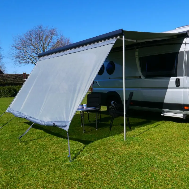 Frontal de toldo your GEAR Sun + Rain Blocker de 3,7 x 2 m instalado en una autocaravana, mostrando la tela doble para protección solar, viento y lluvia, montada en área de camping sobre césped.