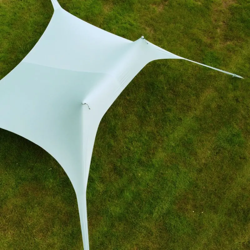 Abri de plage your GEAR Cameo 3x3m XXL en lycra, monté sur gazon, forme carrée tendue avec coins fixés au sol, offrant une grande zone d’ombre et protection UV 50+ pour plage ou pique-nique.
