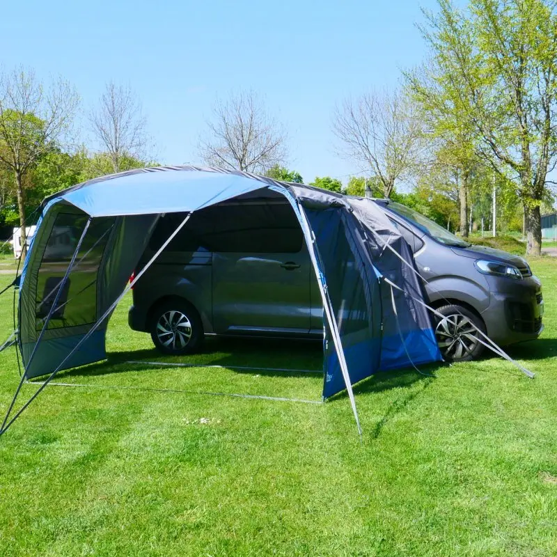 Busvorzelt your GEAR Panarea 320, aufgebaut an einem grauen Van auf Wiese, mit großem, offenen Sonnendach, seitlichen Eingängen und robusten Stangen; UV-Schutz 50+, wasserdicht.