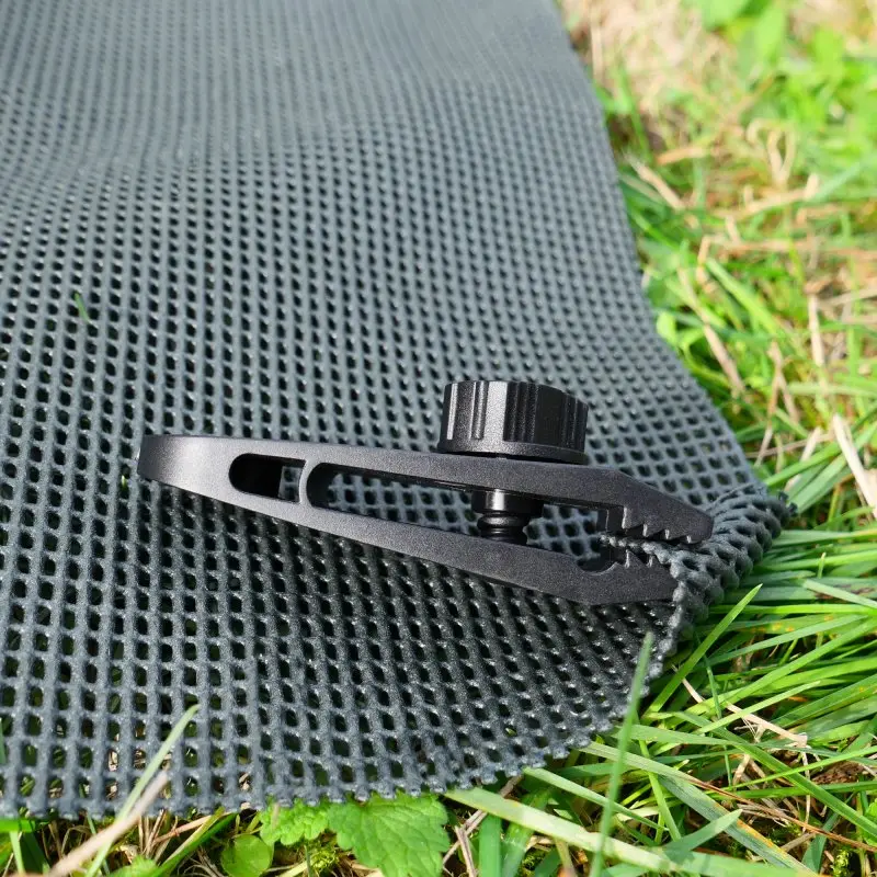 Tapis de sol your GEAR 300 x 600 cm, structure à mailles ouvertes, revêtement mousse doux, montré sur l’herbe avec une pince de fixation noire, idéal pour auvent, perméable à l’air et à l’eau.