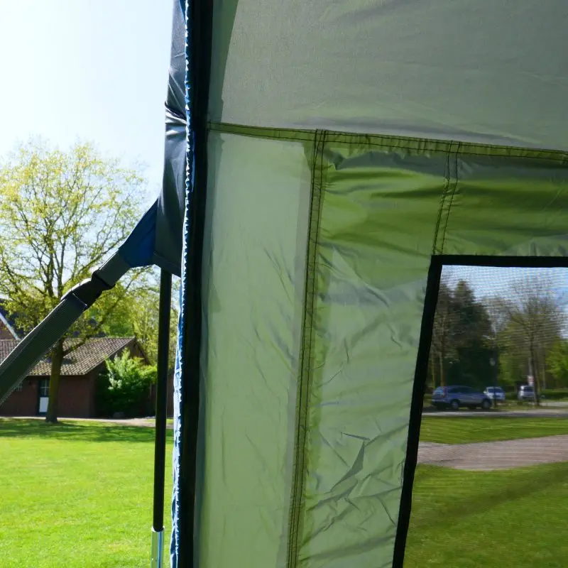 Partie latérale du auvent your GEAR Panarea 320 pour van, montrant la fixation par sangle, la fenêtre avec moustiquaire et le tissu imperméable vert clair, monté en extérieur sur une aire de camping.
