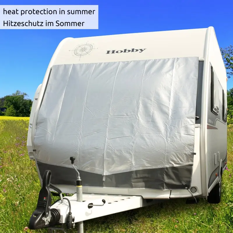 Wohnwagen mit your GEAR Thermo-Bugschutzplane 240 x 160 cm, silberne Aluminiumbeschichtung außen, schützt Front vor Sonne und Frost, befestigt am Caravan, auf Wiese bei blauem Himmel.