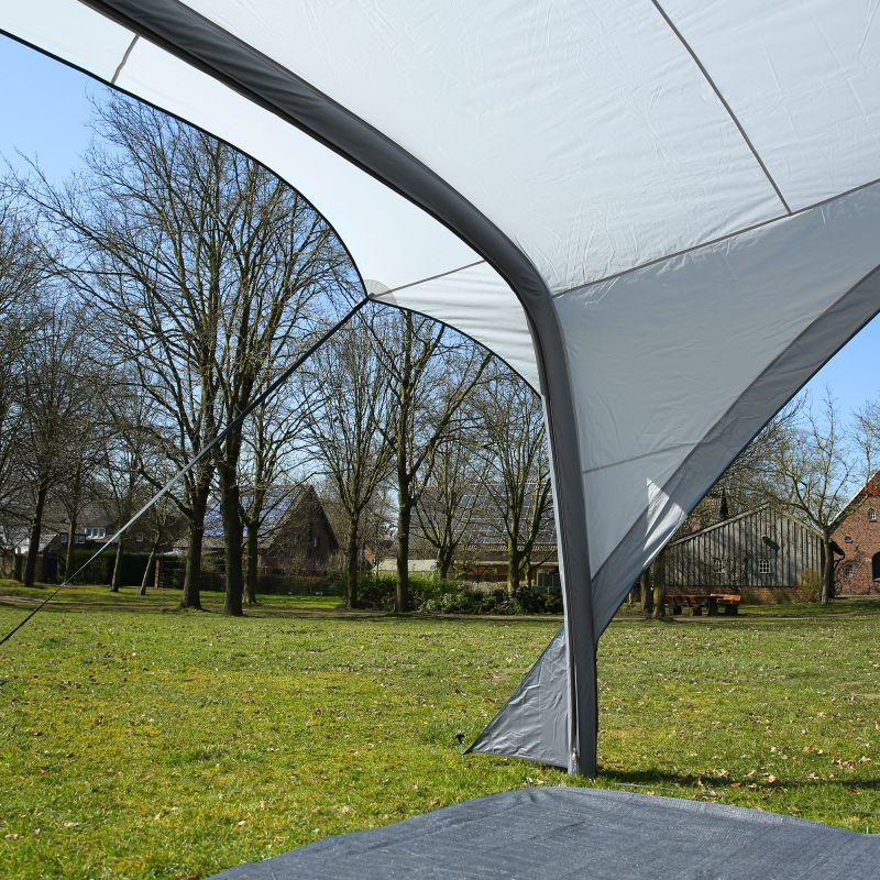 Auvent gonflable your GEAR Caravan Amalfi Air 3.6 gris clair avec boudins d'air sombres, tissu UV50+ tendu, haubans et piquets ancrés sur pelouse, vue rapprochée de la voûte et de la jonction au sol.