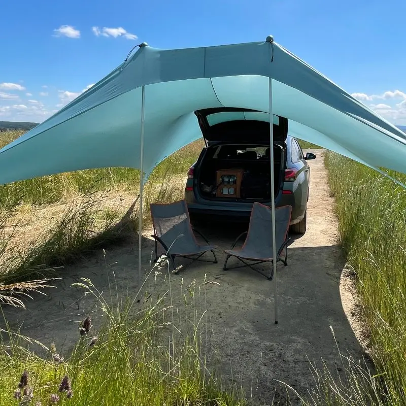 XXL your GEAR Cameo beach shelter, 3x3 m, light blue Lycra sunshade with UV 50+ protection, set up outdoors beside a car with two camping chairs underneath, ideal for beach or picnic.