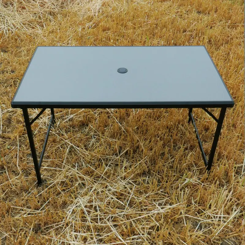 Table de camping your GEAR Tivoli XL, 120x70 cm, plateau gris en aluminium, pieds pliables noirs, résistant à l’eau, léger, idéal pour extérieur, jardin ou voyage, posé sur un champ de blé coupé.