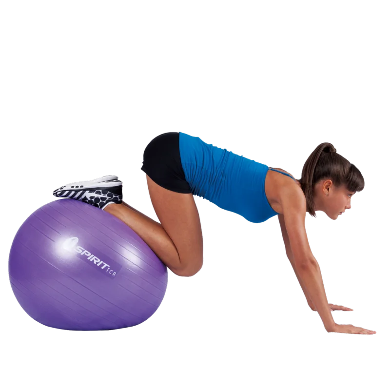 Woman exercising on a purple Spirit TCR gym ball, 65 cm diameter, wearing sportswear. The fitness ball is used for balance and core training, suitable for yoga, fitness, and as an office chair alternative.