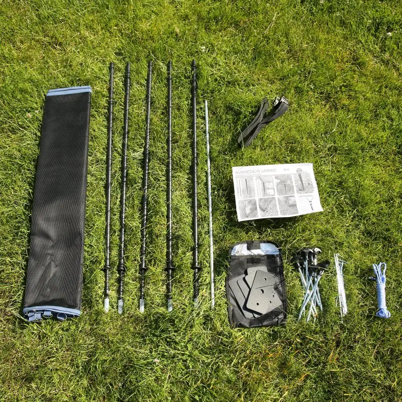 your GEAR Larino 400 portable dog fence set on grass, showing black carrying bag, five fence poles, straps, instructions, pegs, mounting plates, blue rope, and accessories for modular assembly. Ideal for camping or garden.
