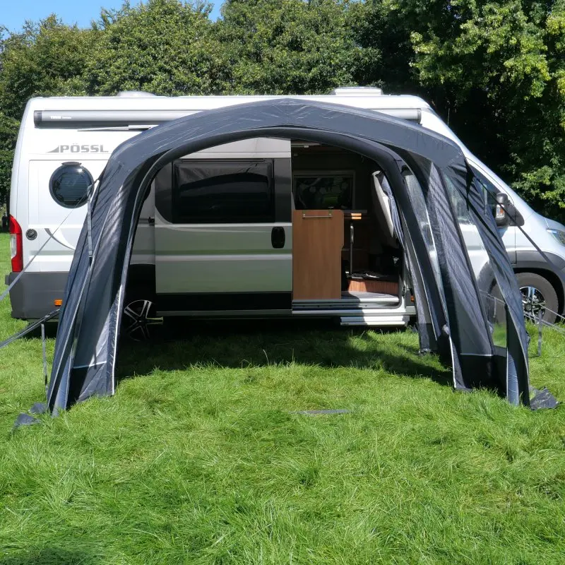 Vorzelt your GEAR Manarola Air, aufblasbar, 320 x 325 cm, an silbernem Wohnmobil angebracht, seitliche Schleusentür, ideal für Kastenwagen mit Schiebetür, auf grünem Gras, Campingumgebung.