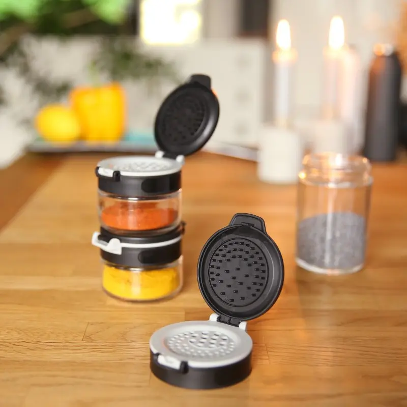 Set de 10 pots à épices en verre your GEAR Double-Flip, 85 ml, couvercles noirs à double ouverture avec tamis, empilables, format plat idéal pour tiroirs, visibles avec épices colorées sur une table en bois.