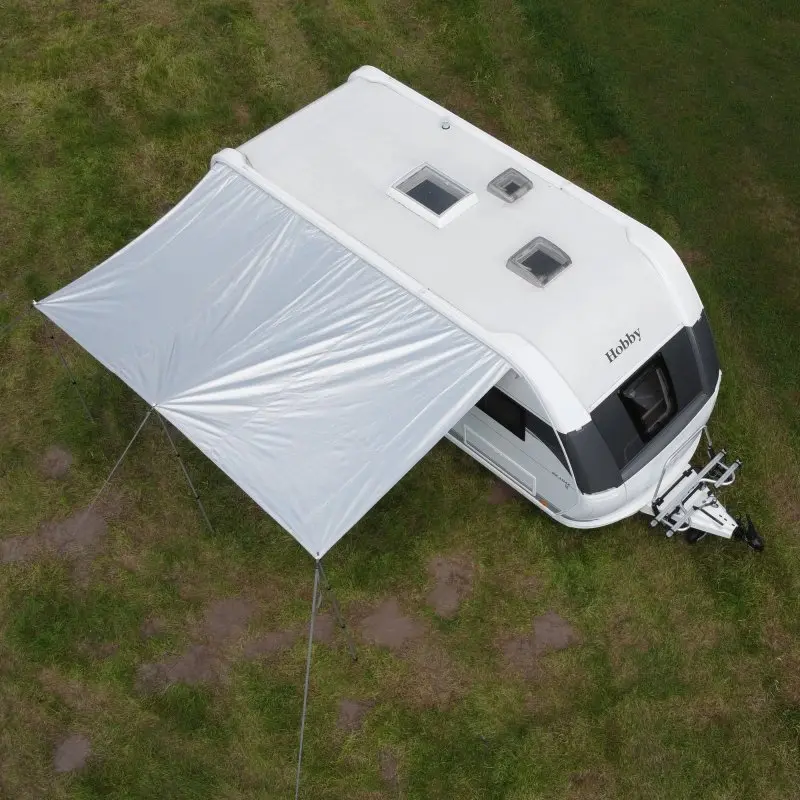 your GEAR caravan thermo tarp 435 x 250 cm with reflective aluminum coating, UV80 sun protection, and waterproof material, attached to a white caravan as a sun canopy on a grassy campsite.