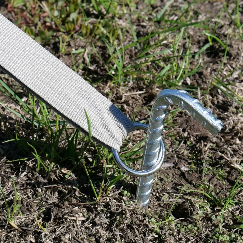 Ancrage au sol du pavillon your GEAR Sonora, sangle beige robuste fixée par un piquet en métal dans la terre, assurant la stabilité du grand chapiteau en coton pour une protection solaire fiable.