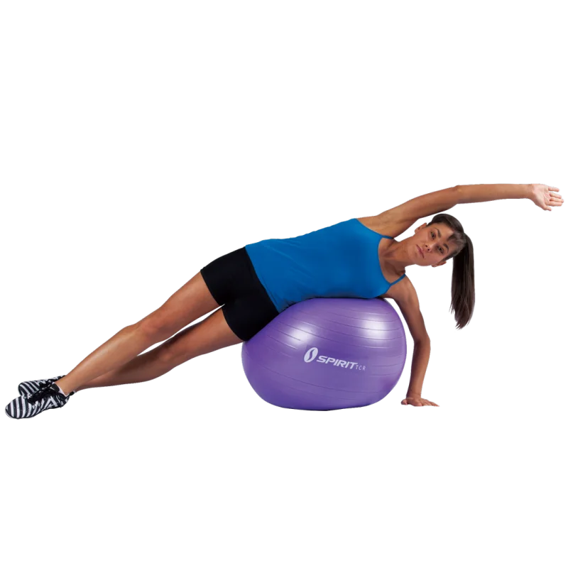 Woman exercising on a purple Spirit TCR gym ball, 65 cm diameter, wearing athletic clothes. The fitness ball is used for core and balance training, suitable for yoga, pilates, and office chair alternative.