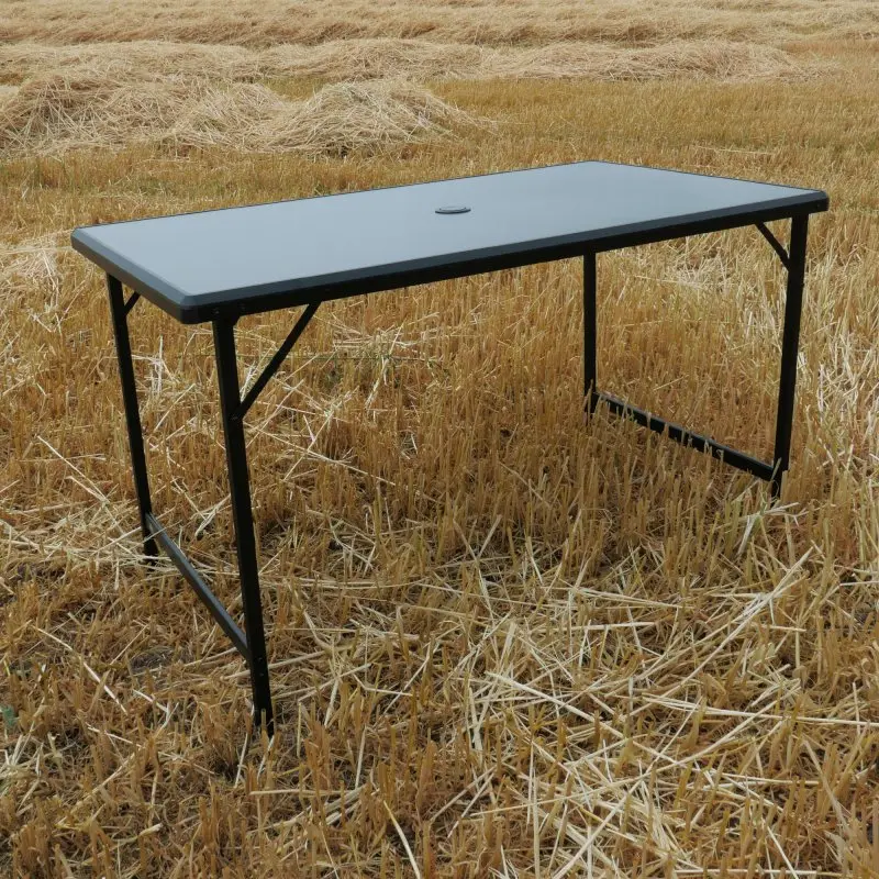 Table de camping your GEAR Tivoli XL 120x70 cm, structure pliante en aluminium, plateau rectangulaire gris, résistant à l’eau, posé sur un champ, idéal pour extérieur et jardin.