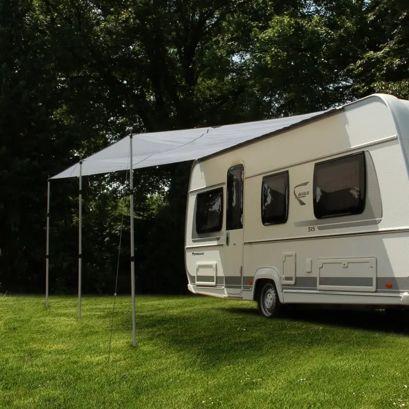 Toldo para caravana your GEAR de 4,5 x 2,4 m en color gris, instalado con 3 postes de aluminio junto a una caravana, proporcionando sombra y protección solar UV 50+ sobre césped verde.