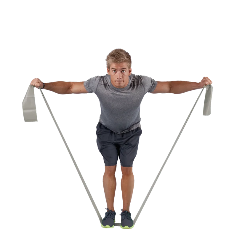 Man exercising with Spirit Fitnessband, latex-free resistance band (183x10 cm, 22.5 kg strength), performing shoulder workout. The grey gym band is stretched between his hands and under his feet.
