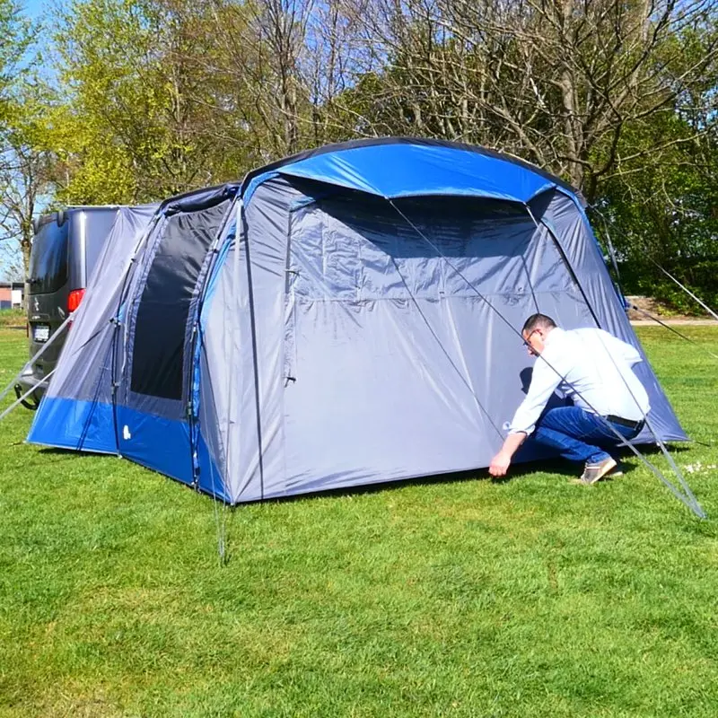 Busvorzelt yourGEAR Panarea 320 mit geschlossener Vorderwand und Zeltbodenplane, befestigt an einem Van. Sichtbar sind Reißverschlüsse, Fenster und wetterfeste Materialien in Blau-Grau. Outdoor-Aufbau auf Wiese.
