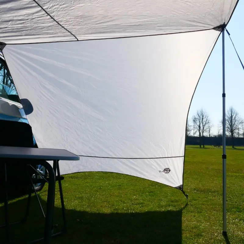 Grau-weißes your GEAR Tropea Bus Vorzelt mit UV 50+ Sonnensegel und Seitenwänden, befestigt an einem Van, auf einer Wiese aufgebaut, zwei Aluminium-Teleskopstangen sorgen für Stabilität.