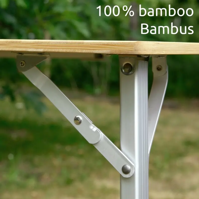 Detailaufnahme eines your GEAR Portofino M Campingtischs mit 1,2 cm starker Tischplatte aus 100 % Bambus, silbernen, höhenverstellbaren Teleskopbeinen und Scharnieren, Text "100% bamboo Bambus" im Bild.