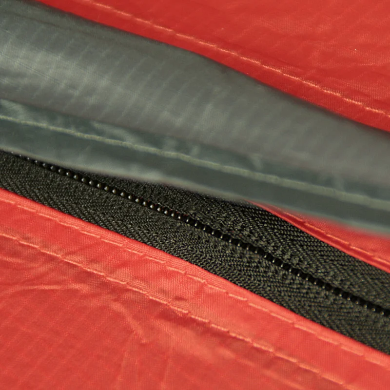 Gros plan sur la fermeture éclair étanche et la couture renforcée du tissu rouge du 10T Zelt Silicone Valley, tente trekking 3 personnes, matériau siliconisé imperméable 5000 mm pour camping.