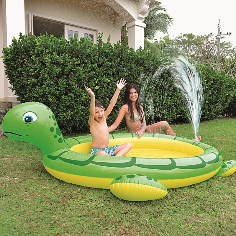 Piscine gonflable Jilong en forme de tortue, 215x189 cm, avec fonction arroseur, enfants jouant et s’amusant dans le jardin, design coloré, raccordement pour tuyau d’arrosage visible.