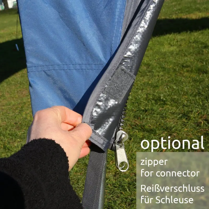 Main de personne ouvrant une fermeture éclair sur la toile bleue imperméable du pavillon your GEAR Bergamo 430, montrant l’option de raccordement pour bus ou camping-car, sur fond d’herbe verte.
